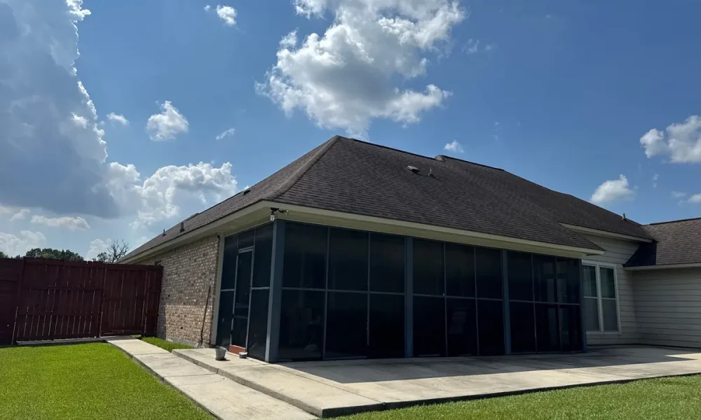 Back of a Central, Louisiana home with a long screened porch and the original dark asphalt shingles, photographed before the roof replacement
