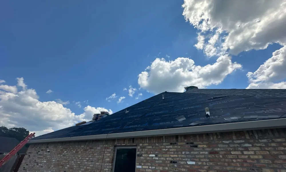 Side roof plane covered in synthetic underlayment above a brick wall, partway through the install