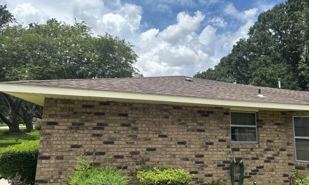 Side of a single-story brick home in Baker, Louisiana with its original brown shingle roof before replacement
