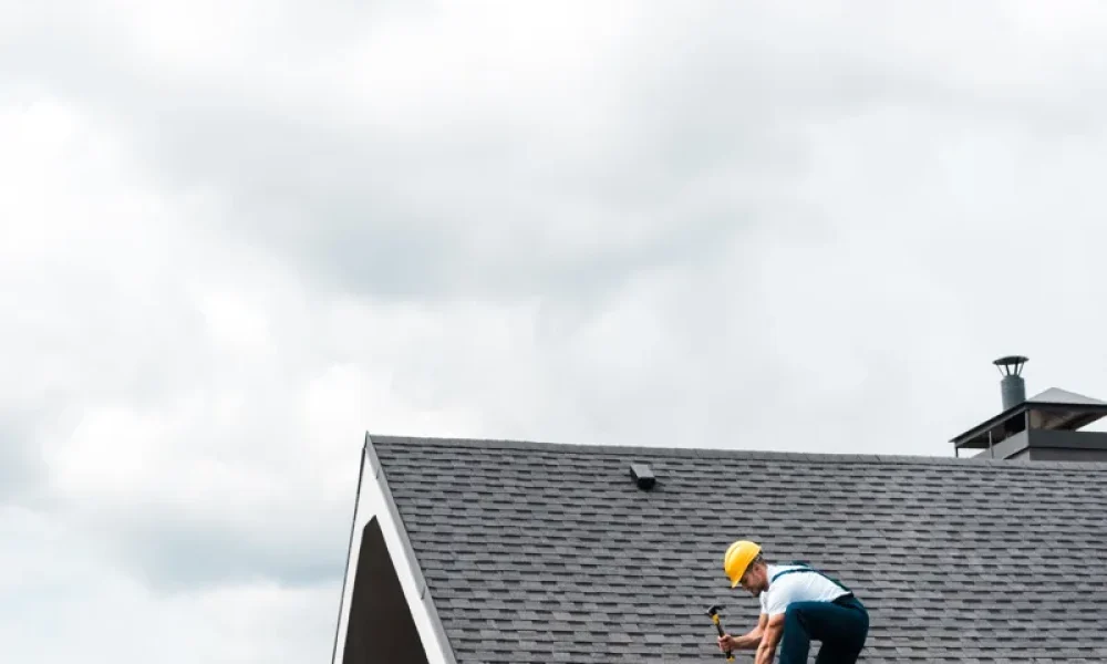 repairman in yellow helmet repairing roof with gray shingles