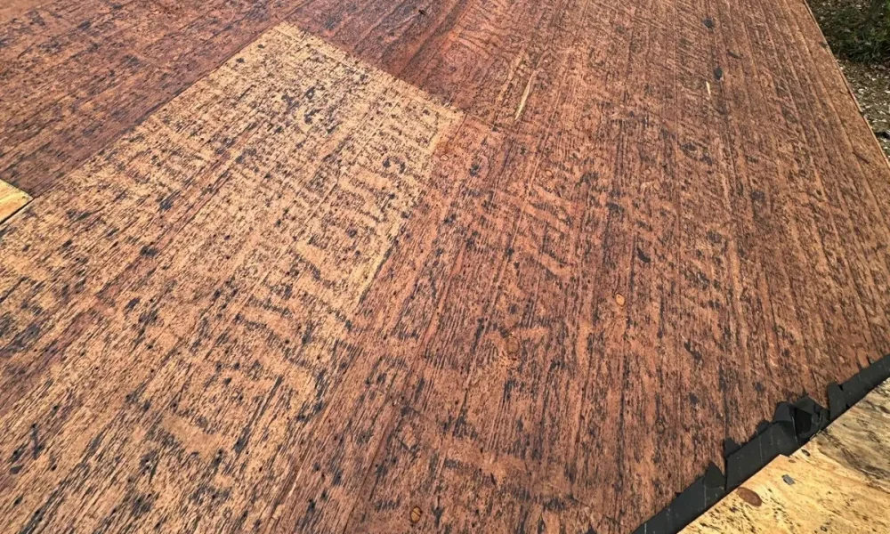 Old board roof decking exposed after shingle tear-off on a Baker, Louisiana home, with new plywood patches