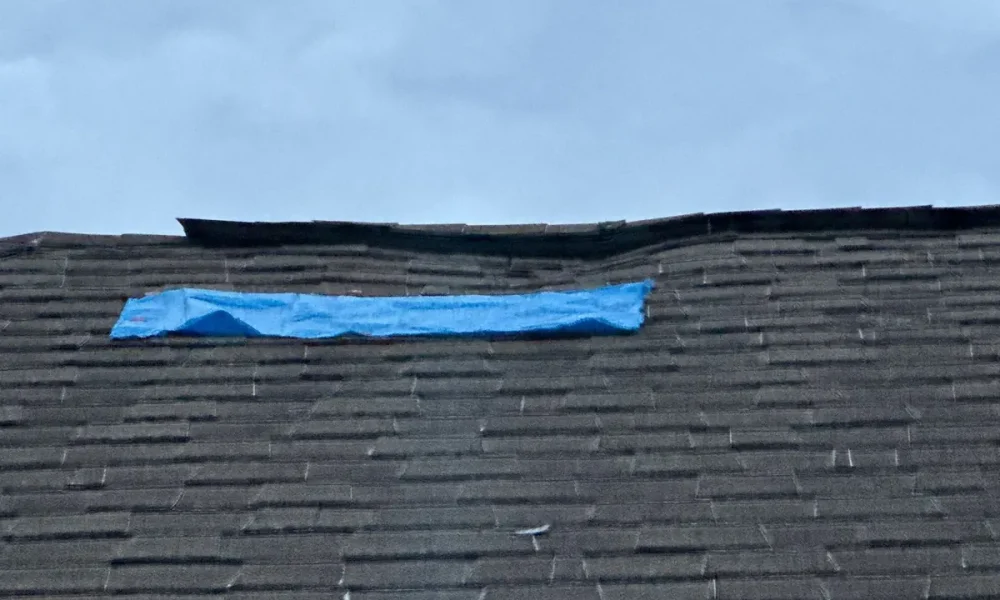Blue tarp covering a damaged section near the ridge of the old shingle roof on a Greenwell Springs, LA home before replacement