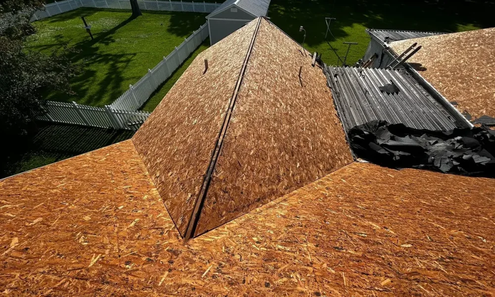 Bare OSB roof decking on a hip roof during the Roof Rescue tear-off in Greenwell Springs, LA, beside a low-slope metal panel section