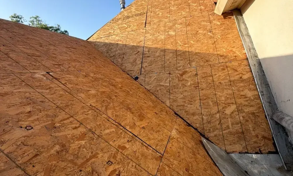 Bare roof deck after tear-off along the stucco wall, with the old wall flashing still in place