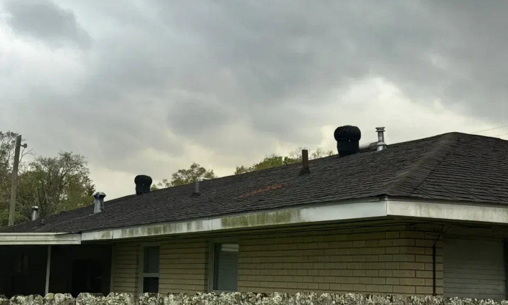 Older dark shingle roof with turbine vents on a single-story brick home in Central, LA before the metal roof