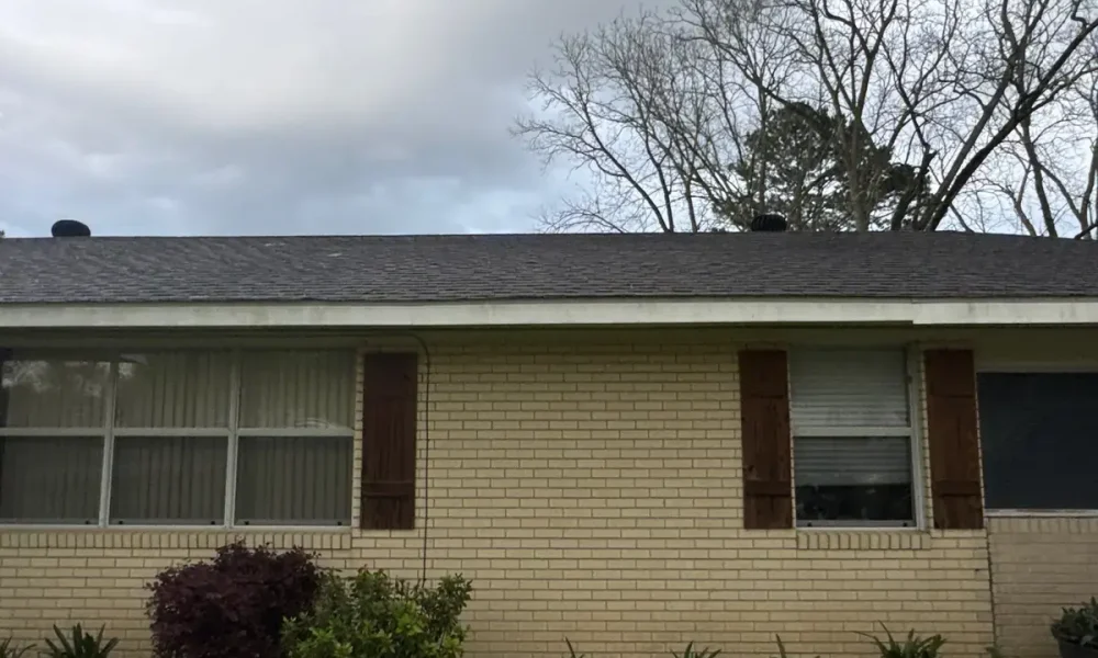Side of a cream brick home in Central, LA with its original dark shingle roof