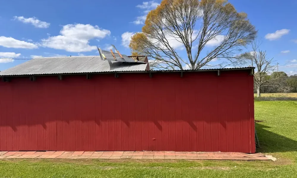 Red barn-style shop in Zachary, LA with its corrugated metal roof peeled back near the peak