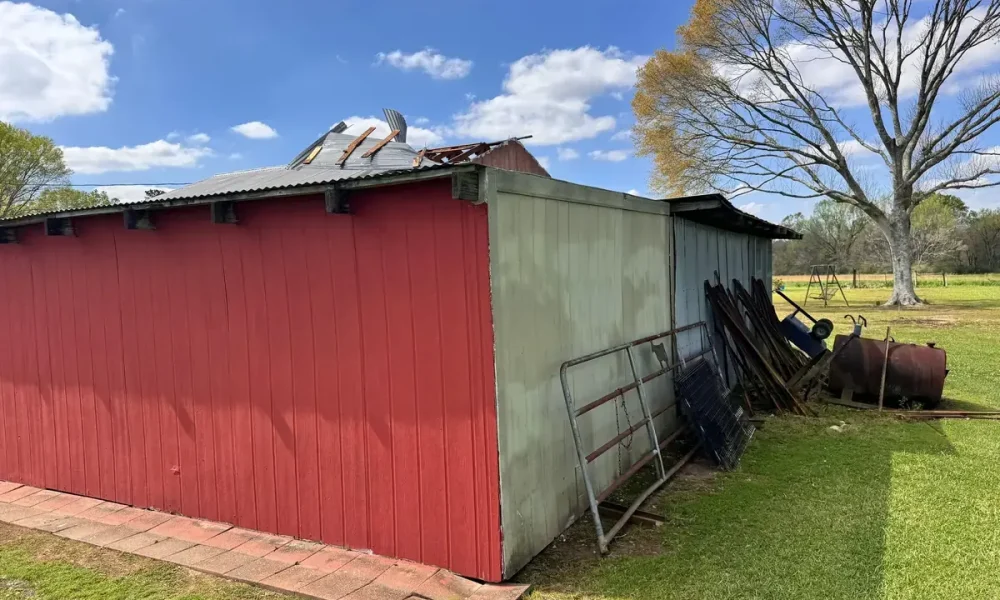 Corner of a Zachary, LA shop with torn corrugated roofing and broken lats at the peak