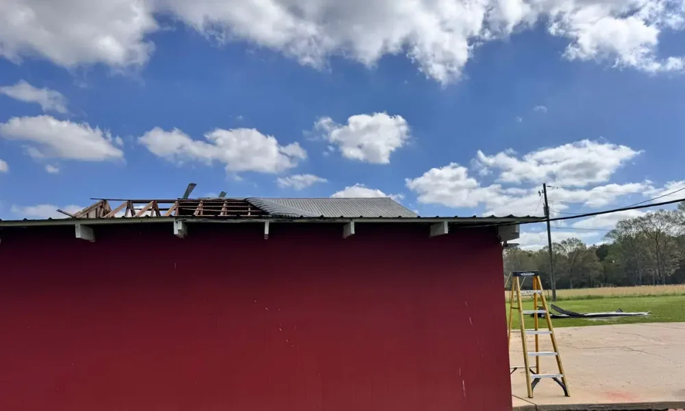 Torn-open metal roof and exposed framing on a red shop building in Zachary, LA